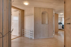 Quarto com paredes de madeira, um suporte de metal e uma porta que dá para uma cozinha.