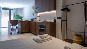 A modern kitchen with wooden cabinets, a microwave, and a kettle. There is a dining area with a table and chairs, and a large window providing natural light. - VLC HOST - Luz Casanova E (Valencia)