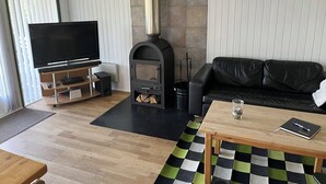 A living room with a TV, fireplace, black leather sofa, wooden coffee table, and a patterned rug.