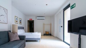 A hotel room with a bed, a sofa, a TV, and a door with an exit sign. - VLC HOST - Luz Casanova B (Valencia)