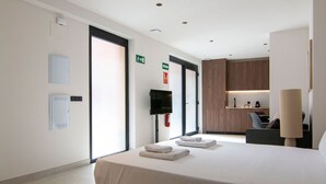 A hotel room with a bed, a desk, a chair, a TV, and a bathroom visible through an open door. - VLC HOST - Luz Casanova B (Valencia)