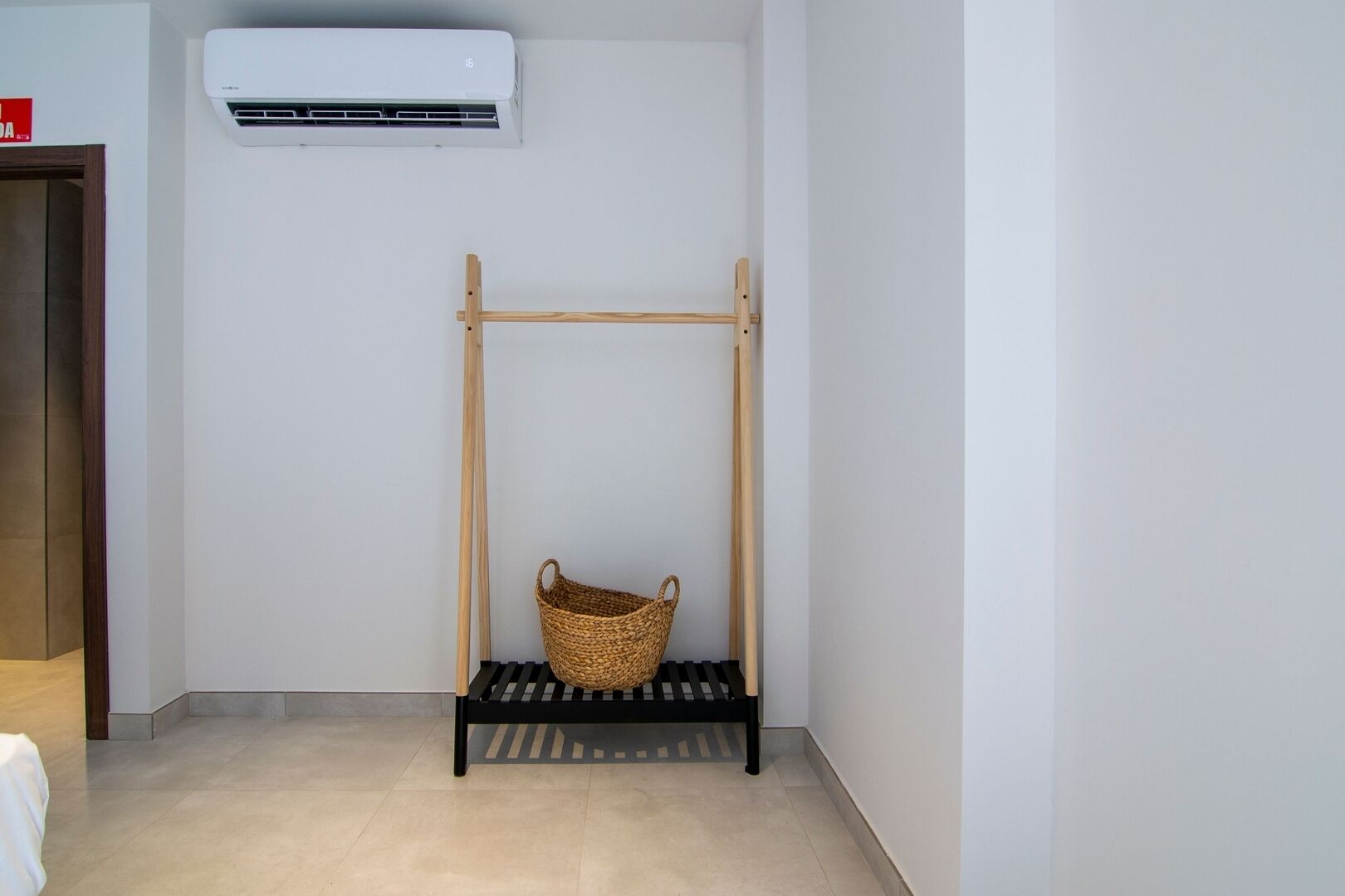 A corner room with a black metal bench, a woven basket, and a white air conditioning unit mounted on the wall.