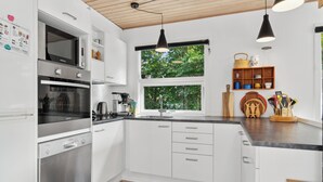 Una cocina moderna con armarios blancos, electrodomésticos de acero inoxidable, un ventanal grande y una lámpara colgante negra.