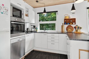 A modern kitchen with white cabinets, stainless steel appliances, a large window, and a black pendant light.