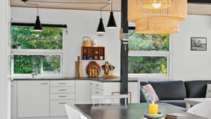Una cocina moderna con armarios blancos, una isla de madera, lámparas colgantes y vistas al exterior.