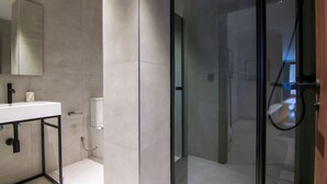 A modern bathroom with a glass shower enclosure, a white sink with a marble countertop, and a large mirror. - VLC HOST - Luz Casanova C (Valencia)