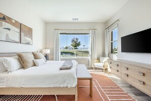 A modern hotel room with a large bed, a flat-screen TV, a desk, and a view of the outdoors.