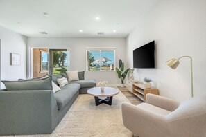 A modern living room with a sectional sofa, a round coffee table, and a flat-screen TV mounted on the wall.