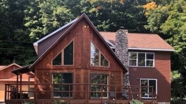 A wooden cabin with a stone chimney, large windows, and a porch. - Large 6-bedroom home, sleeps 16! WiFi and a private sandy beach in Traverse City (Traverse City)