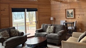 A cozy cabin interior with wooden walls, two sofas, a coffee table, and a dining table with chairs. - Large 6-bedroom home, sleeps 16! WiFi and a private sandy beach in Traverse City (Traverse City)