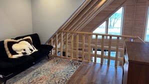 A room with a black sofa, a patterned rug, a wooden staircase, and a view through a window. - Large 6-bedroom home, sleeps 16! WiFi and a private sandy beach in Traverse City (Traverse City)
