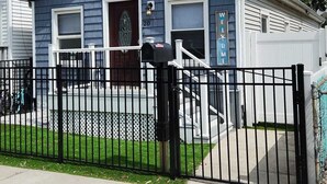 Una casa residencial con fachada azul oscuro, detalles blancos, un porche y una reja de metal negra.