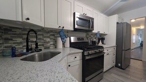 Una cocina moderna con armarios blancos, un microondas de acero inoxidable, una estufa a gas y un refrigerador de acero inoxidable.