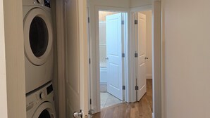 A laundry room with stacked washers and dryers, wooden flooring, and a door leading to another room. - Kensington Area 10 Mins To Downtown! Clean and friendly! Temporary stays!  (Calgary)