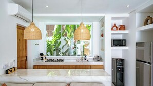 Une cuisine moderne dotée d’un plan de travail en marbre, de deux luminaires suspendus, d’un four encastré, d’un réfrigérateur et d’un distributeur d’eau.