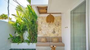 Un espace extérieur moderne, aménagé avec un mur en pierre, un fauteuil suspendu en fibres tressées et une piscine.