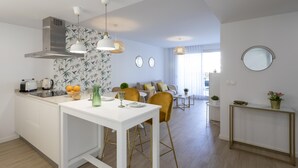 A modern kitchen with white cabinetry, a central island, and pendant lighting. A dining area with a white table and chairs is visible in the background. - Marina Real II, 2 bedrooms, by Bookindenia (Dénia)