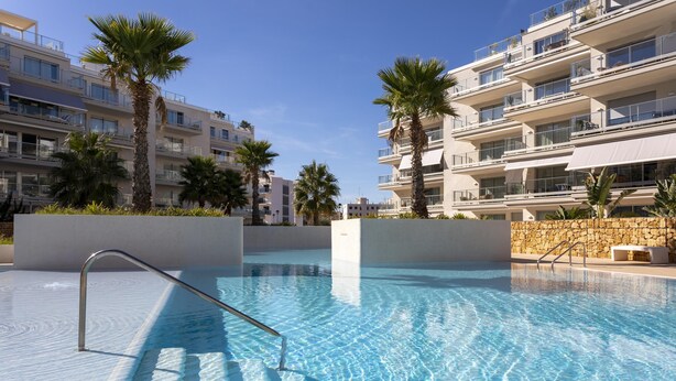 A swimming pool with clear blue water, surrounded by palm trees and modern apartment buildings. - Marina Real II, 2 bedrooms, by Bookindenia (Dénia)