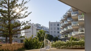 An outdoor seating area with a table and chairs, a hanging chair, and a view of modern buildings in the background. - Marina Real II, 2 bedrooms, by Bookindenia (Dénia)