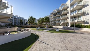 A modern apartment complex with multiple balconies, a landscaped courtyard with artificial grass, and a clear blue sky. - Marina Real II, 2 bedrooms, by Bookindenia (Dénia)