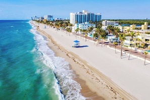 A coastal hotel with a beachfront view, a pool area, and a lifeguard tower.