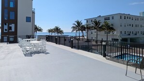 A rooftop terrace with a pool, white chairs, and a view of the beach and ocean.