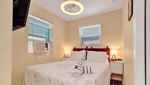 A neatly made bed with a white comforter and a rolled towel, two bedside lamps, and a wall-mounted TV.