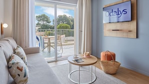 Un soggiorno moderno con divano, un tavolo rotondo, una TV a parete e un balcone con vista sugli alberi.