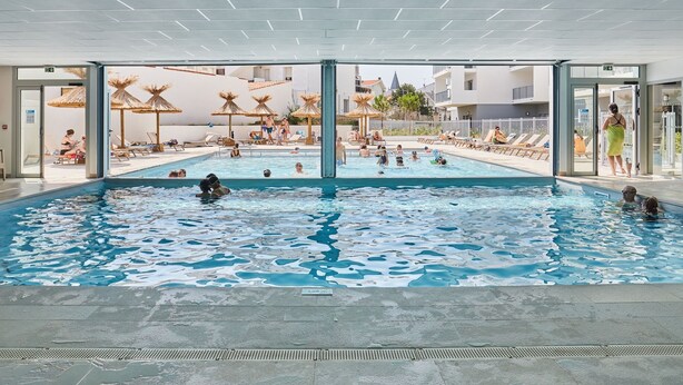 Una piscina interna con acqua cristallina, circondata da sdraio e ombrelloni.