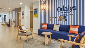 Una hall d'albergo moderna con una parete a righe blu e bianche, un divano blu, sedie in legno e un piccolo tavolino rotondo.