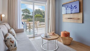 Un salon moderne avec un canapé, une table ronde, un téléviseur fixé au mur et un balcon donnant sur la verdure.