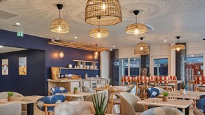 L’intérieur d’un restaurant avec des tables rondes, des luminaires suspendus en osier et une vue sur la rue.