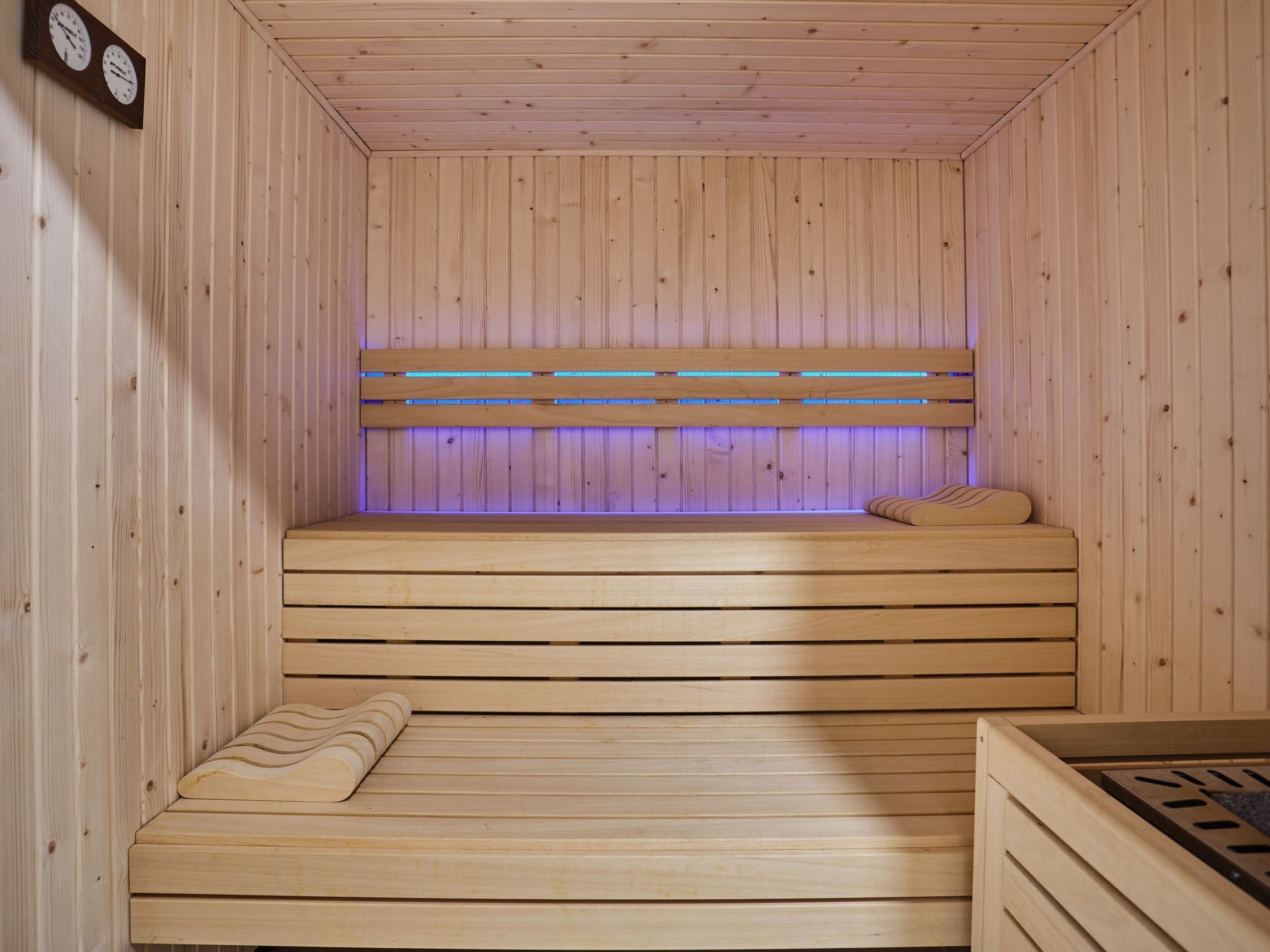 Puinen sauna, jossa on penkki, kaarevaselkänojalla varustettu penkki ja seinälle asennettu kello.