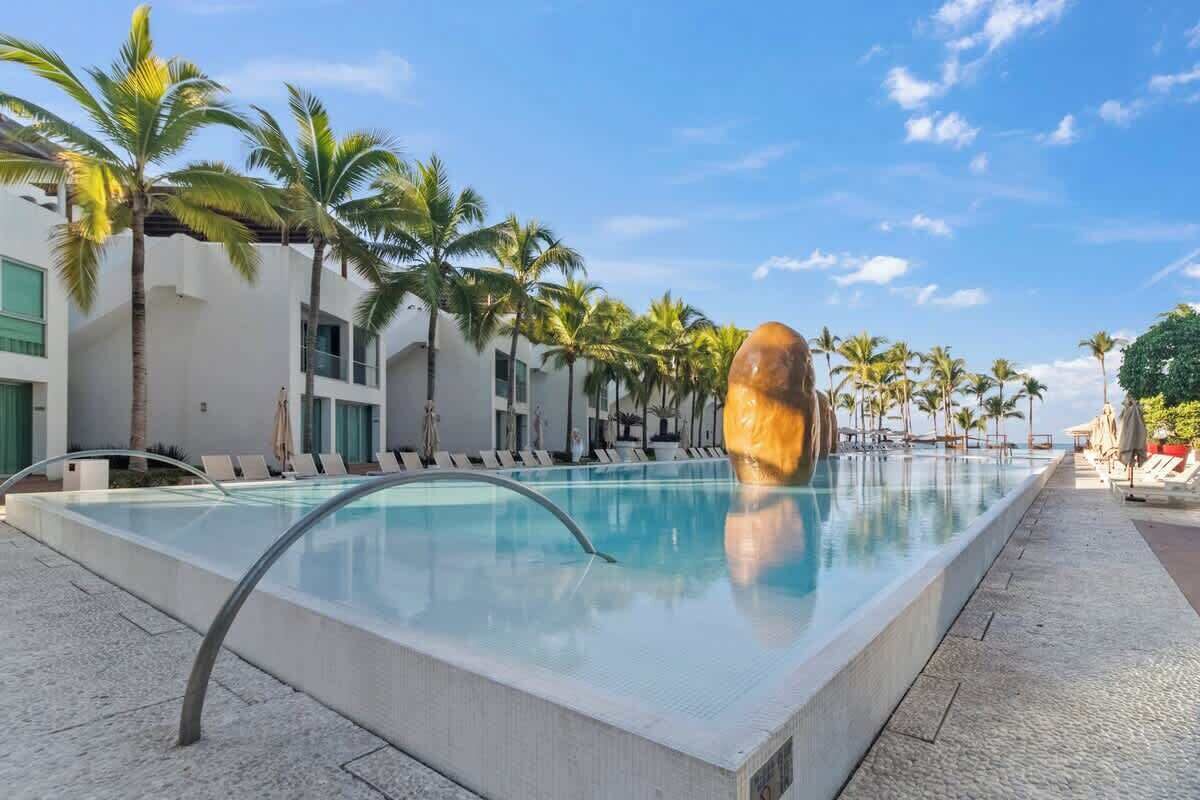 A swimming pool with lounge chairs, palm trees, and a modern building.