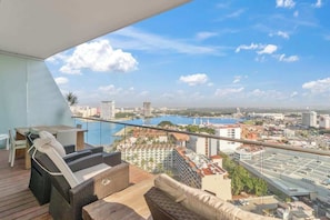 A balcony with wicker furniture, a view of a cityscape, and a body of water.