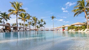 A swimming pool with lounge chairs and umbrellas, surrounded by palm trees. - Luxury Beach Front Condo  21st Floor Views (Puerto Vallarta)