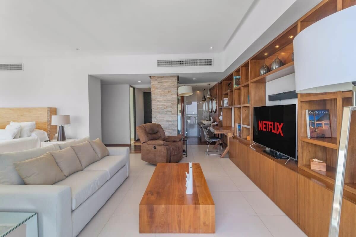 A modern living room with a sofa, a wooden coffee table, a recliner, a TV, and a bookshelf.