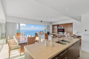 A modern kitchen with a built-in Netflix screen, a dining area with a view of the sea, and a spacious living area.