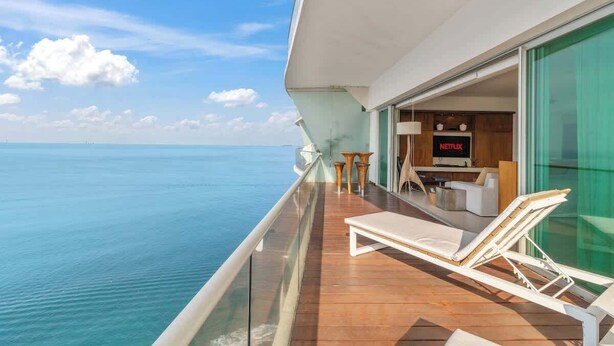 A balcony with a view of the ocean, a lounge chair, a small table, and a sign for Netflix. - Luxury Beach Front Condo  21st Floor Views (Puerto Vallarta)