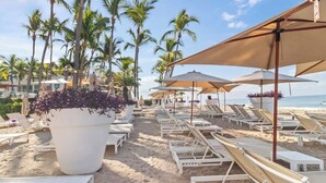 A beach with sun loungers, umbrellas, and a large planter with flowers. - Luxury Beach Front Condo  21st Floor Views (Puerto Vallarta)