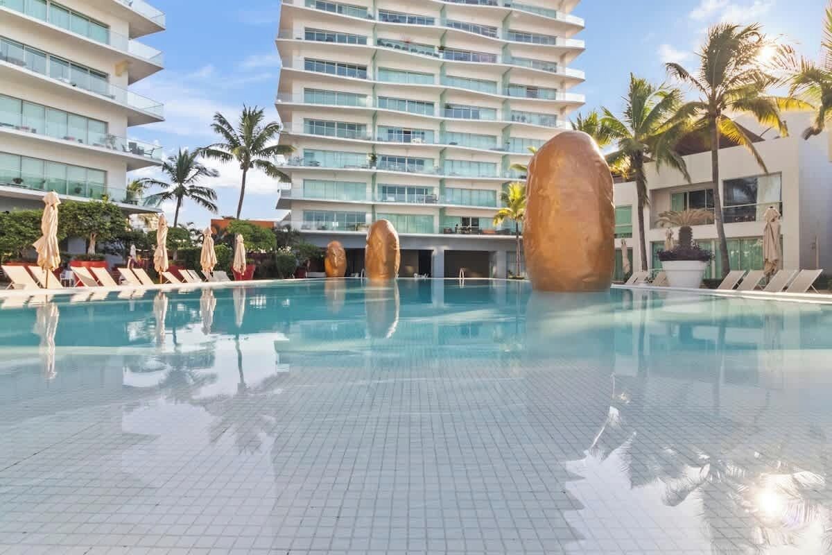 Ein Schwimmbad mit Liegestühlen und Palmen, umgeben von modernen Gebäuden.
