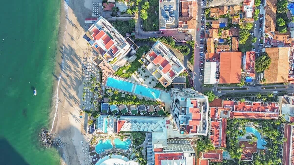 Vue aérienne d’un hôtel situé sur la côte, composé de plusieurs bâtiments, avec une plage et une piscine.