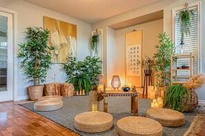 A room with a wooden floor, woven poufs, a table with candles, and various plants.