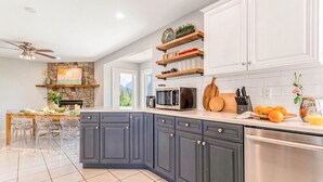 A modern kitchen with dark cabinets, a stone fireplace, and a dining area with a table and chairs. - 180° Amazing View- Ridge Top, 2 Full Kitchen, 3-Level, Sleeps 16 Comfortably (Chilliwack)