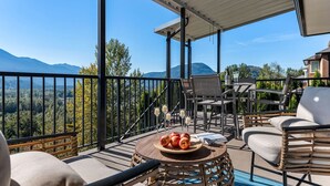 Een balkon met uitzicht op bergen, een tafel met appels en glazen, en tuinmeubilair.
