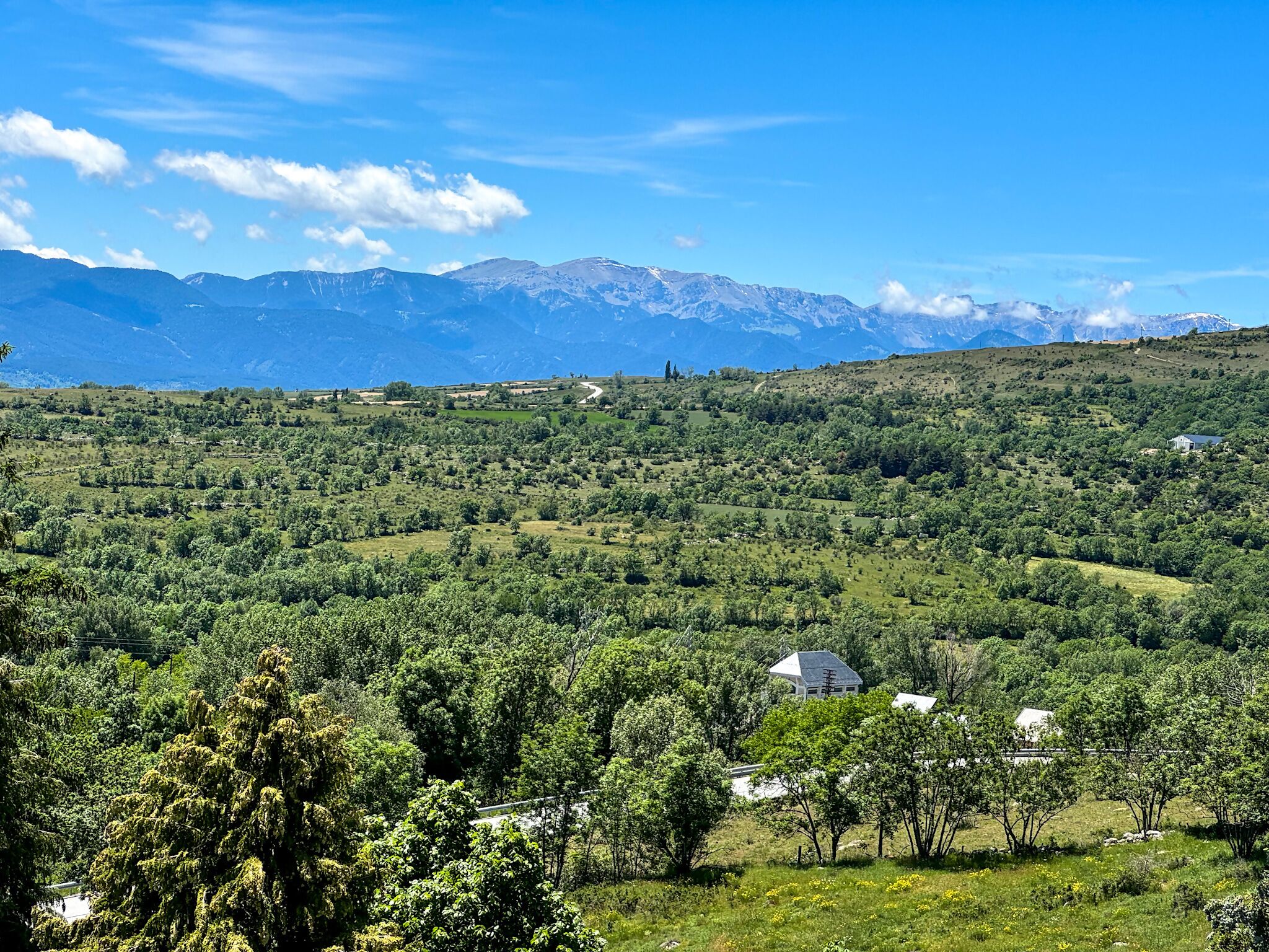 A rural landscape with rolling hills, scattered trees, and a few buildings.