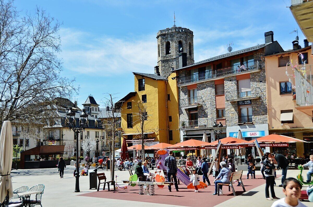 A bustling square with outdoor seating and a historic tower in the background.
