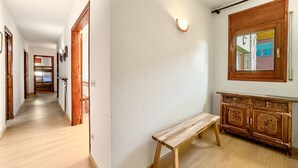 En hall med trägolv, en bänk, ett träskåp med detaljerade sniderier och en väggmonterad lampa.