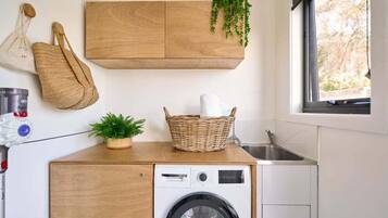 A compact laundry area with a washing machine, a wooden cabinet, a wicker basket, and a hanging plant.