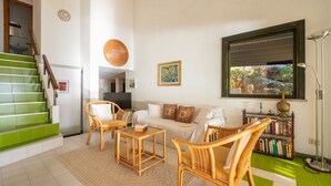 A living room with a sofa, two armchairs, a coffee table, a bookshelf, a television, and a staircase with green steps. - Capo Boi by Interhome (Villasimius)